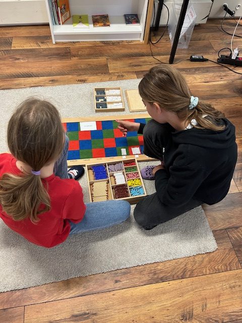 Deux enfants travaillent avec le damier de multiplication Montessori